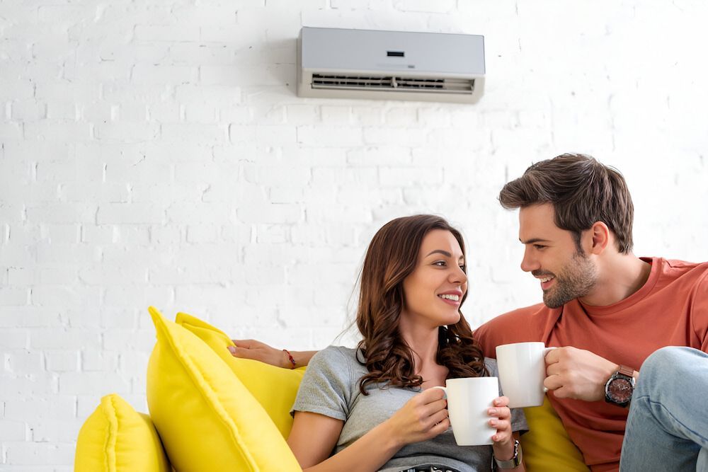 A Man And A Woman Are Sitting On A Couch Drinking Coffee — Mason's Air Conditioning Pty Ltd in Pittsworth, QLD