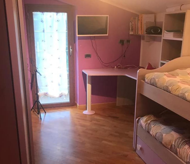 Camera da letto con pareti viola, letti a castello, scrivania, TV e porta-finestra.