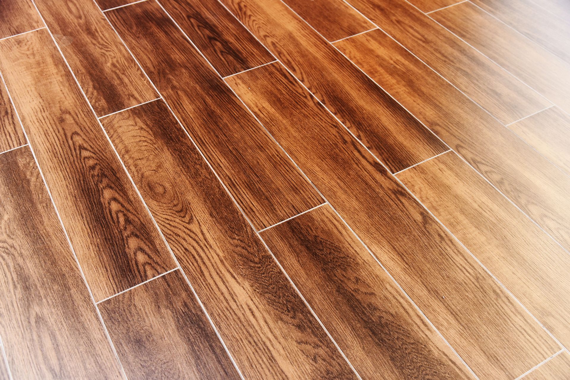 Pavimento in legno, varie tonalità di marrone, con fughe bianche.