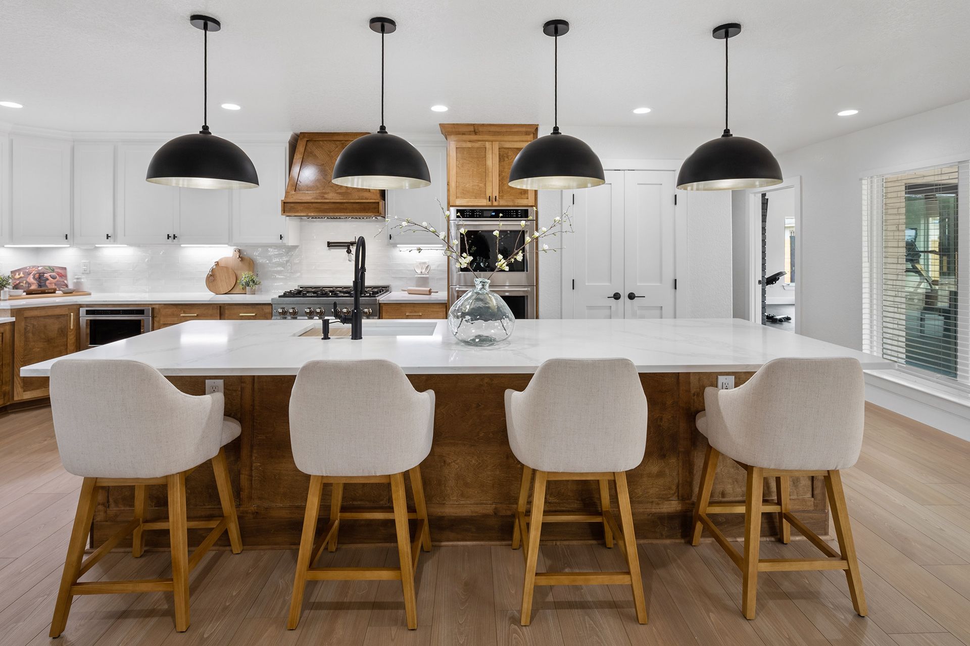 Modern white kitchen with a large island, four beige bar stools, and black pendant lights
