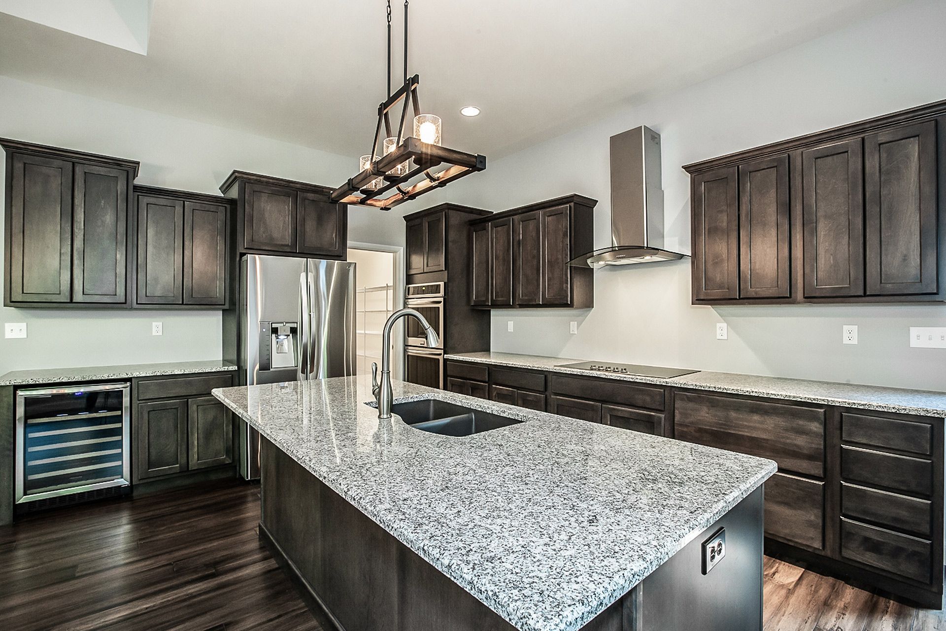 Modern kitchen with dark wood cabinets, a large granite island, stainless steel appliances, and a rectangular pendant light.