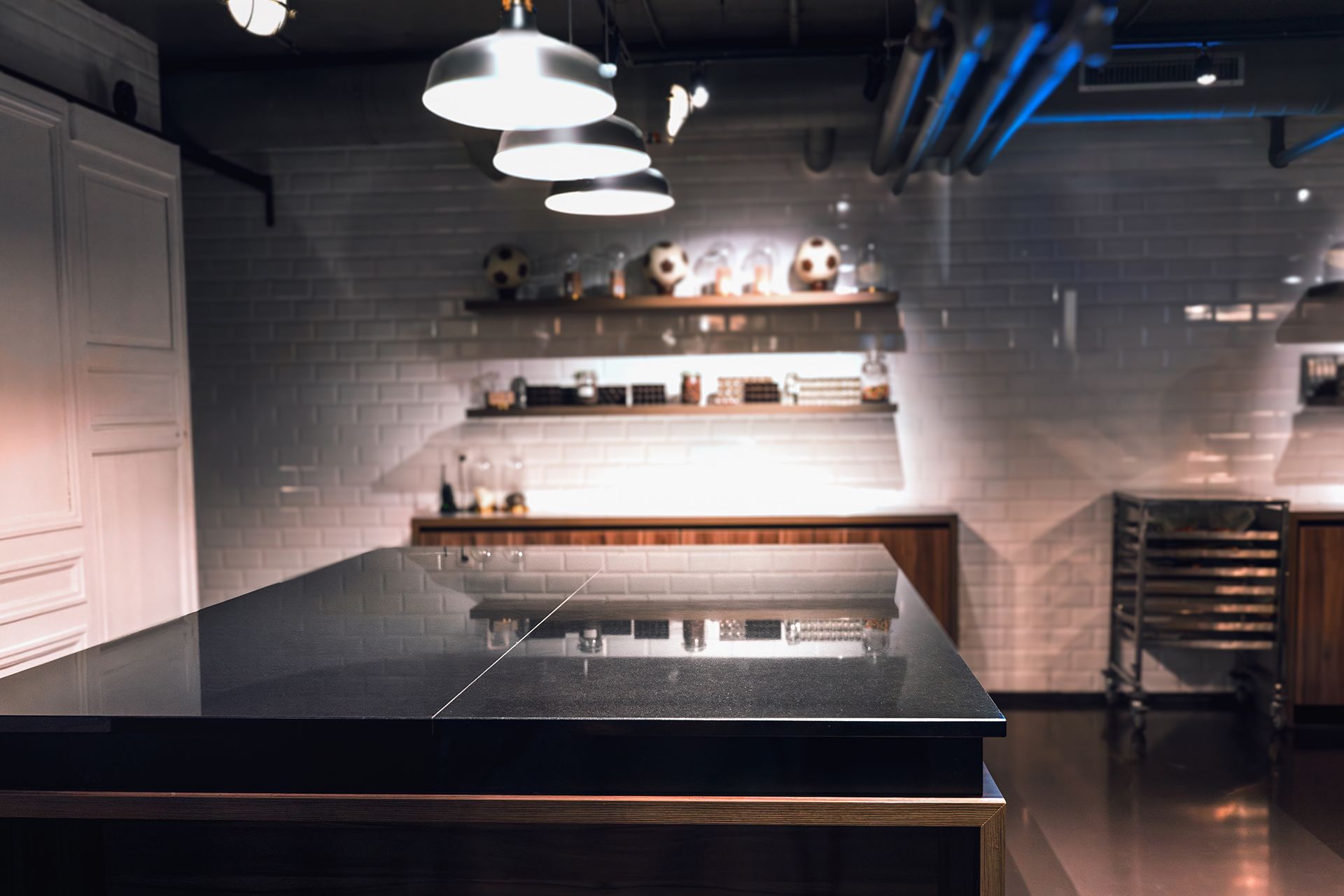 Modern commercial kitchen with hanging lights, stainless steel counters, and wall shelves above a dark island