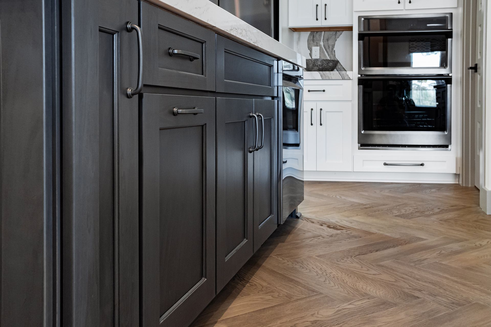 Modern kitchen with dark cabinets, white appliances, and herringbone wood flooring