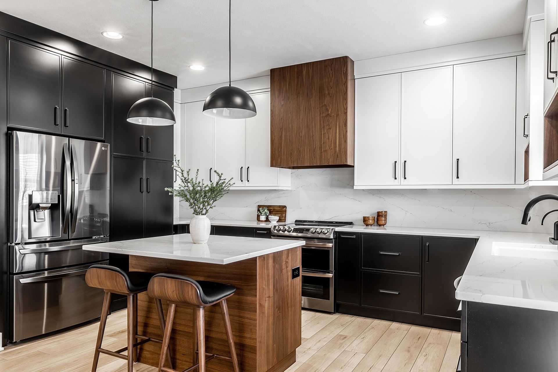 Modern kitchen with a wooden island and hood, black and white cabinets, marble countertops, and two black pendant lights.