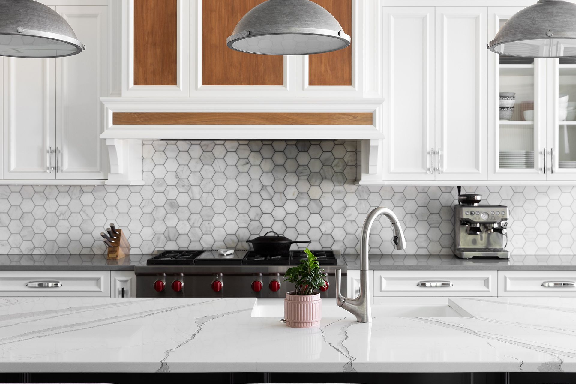 A bright kitchen with white cabinetry, a marble-topped island, a hexagonal tile backsplash, and metallic pendant lights.
