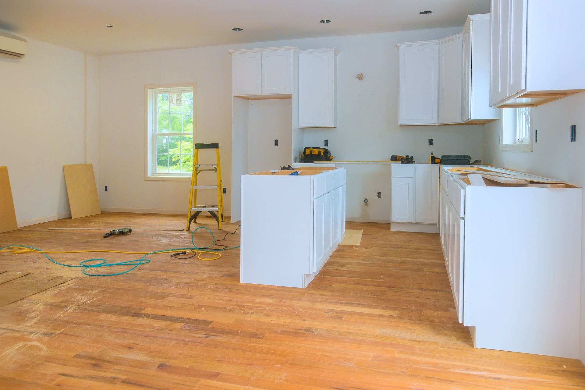 Partially renovated kitchen with white cabinets, wood floors, and tools scattered on the floor