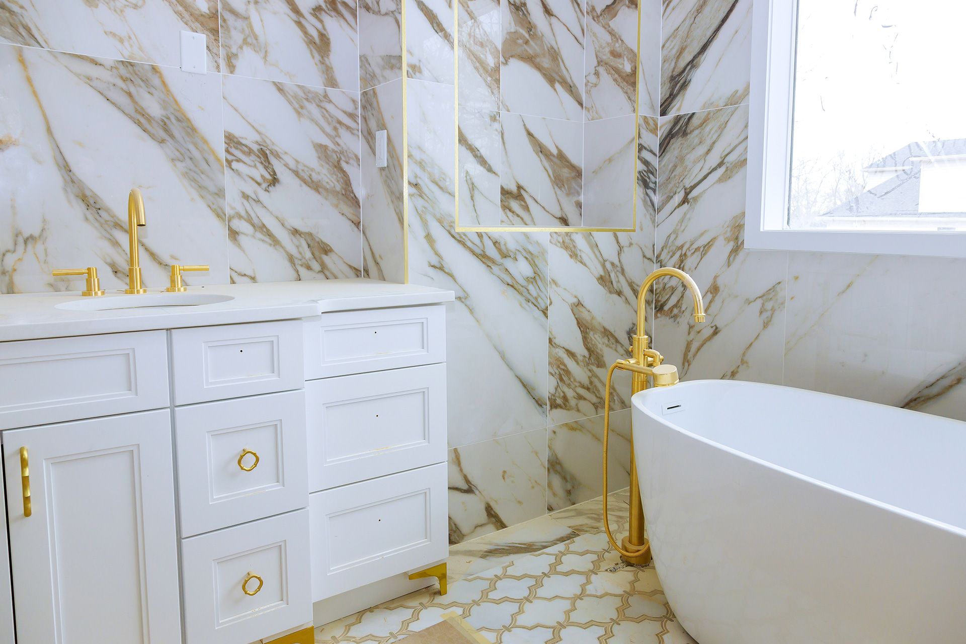 Elegant white-and-gold bathroom with marble walls, gold fixtures, and a freestanding tub