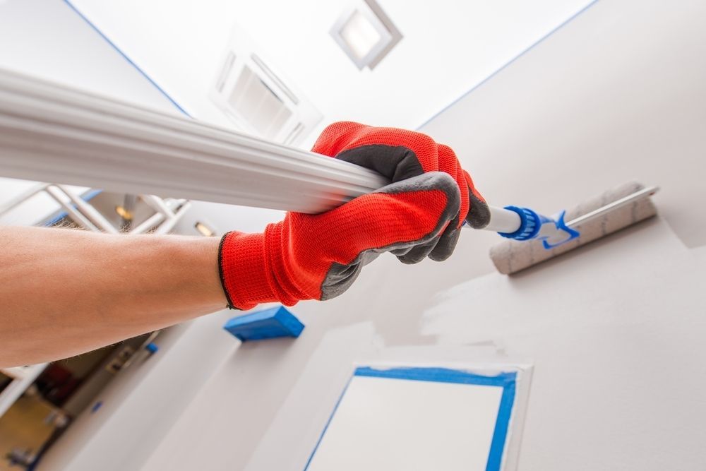 A Person Wearing Red Gloves is Painting a Wall With a Paint Roller — Central Coast Property Maintenance Services In Kariong, NSW