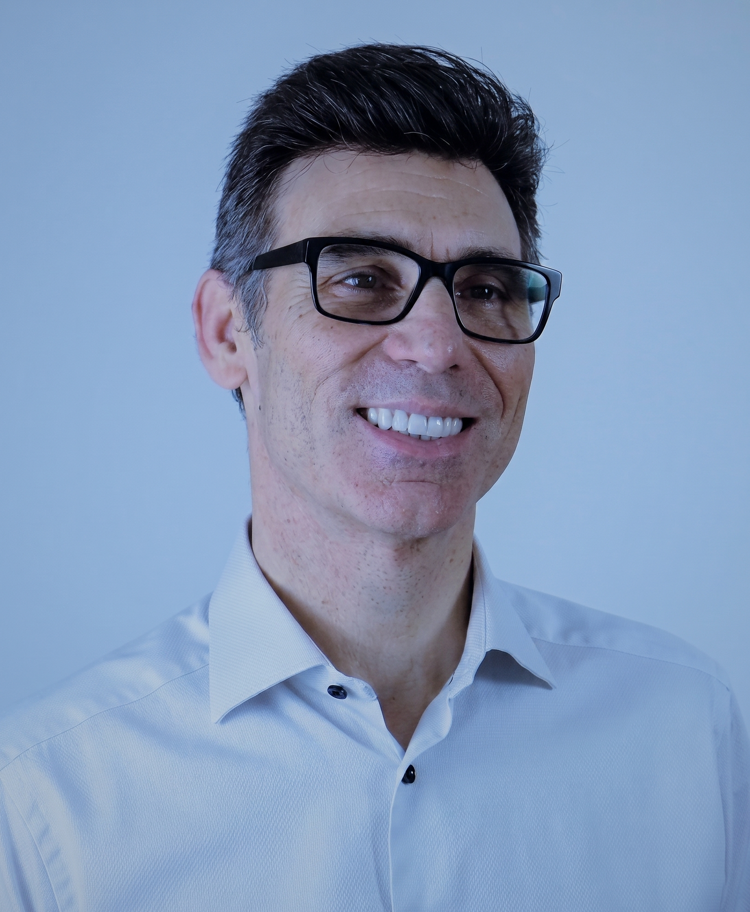 Smiling person wearing glasses and a white shirt against a light blue background