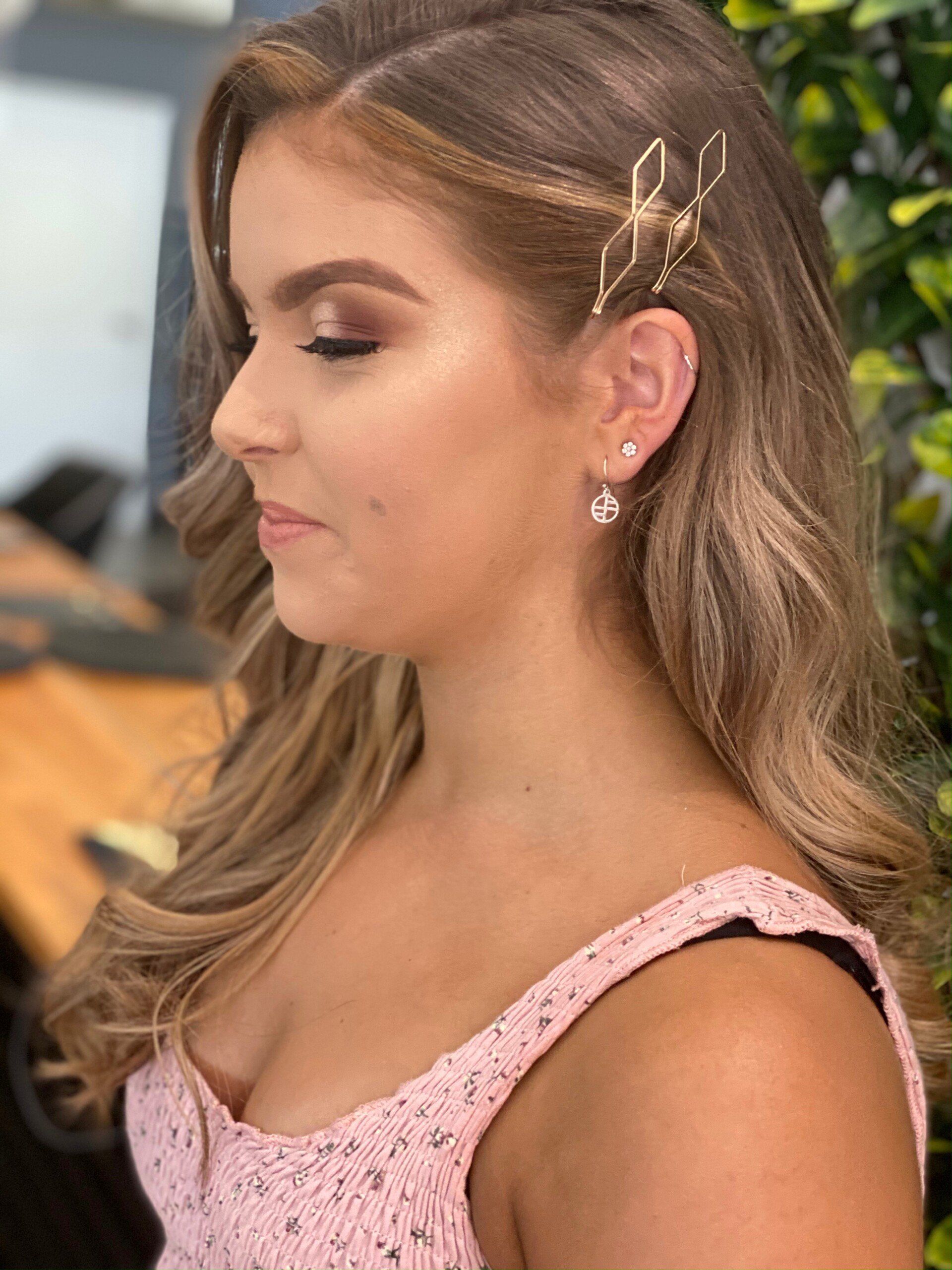 Woman with blonde hair styled with a gold hair accessory, wearing a pink dress and earrings, side profile.