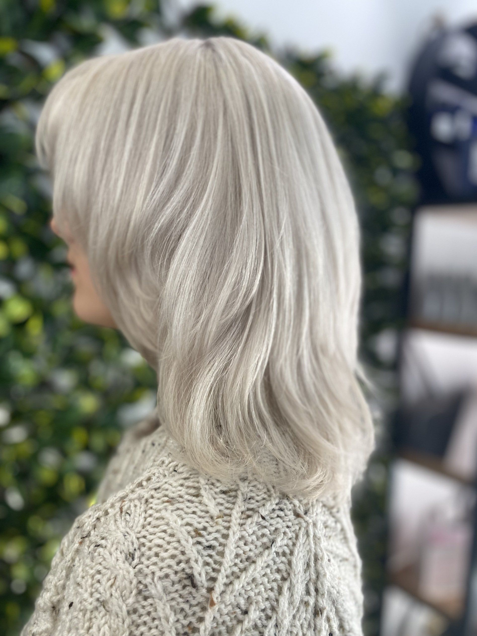 Woman with light-blonde, layered hair, wearing a cream-colored cable knit sweater, side profile.