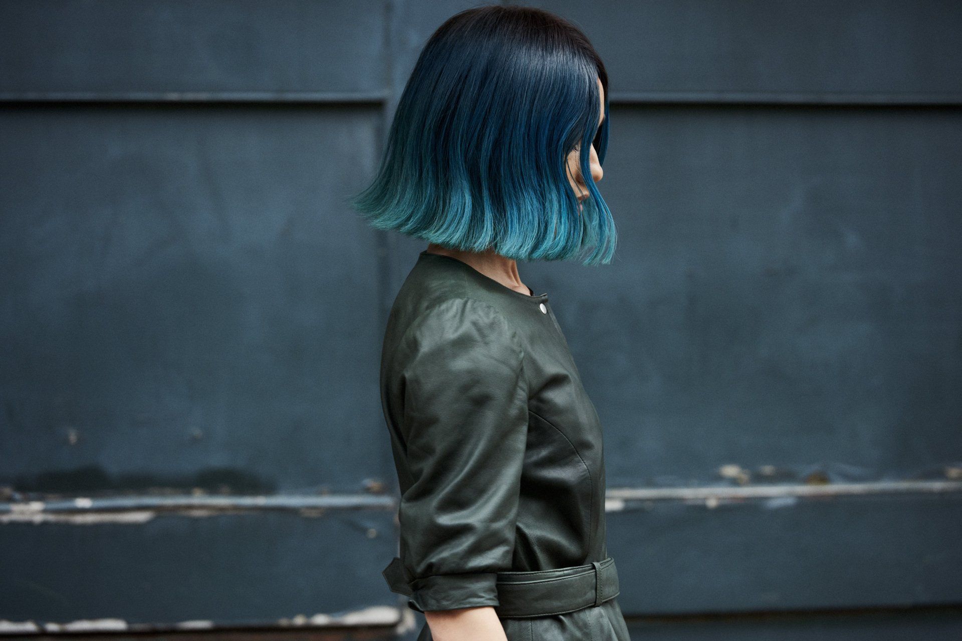 Woman with blue ombre hair and a leather jacket against a dark blue wall.