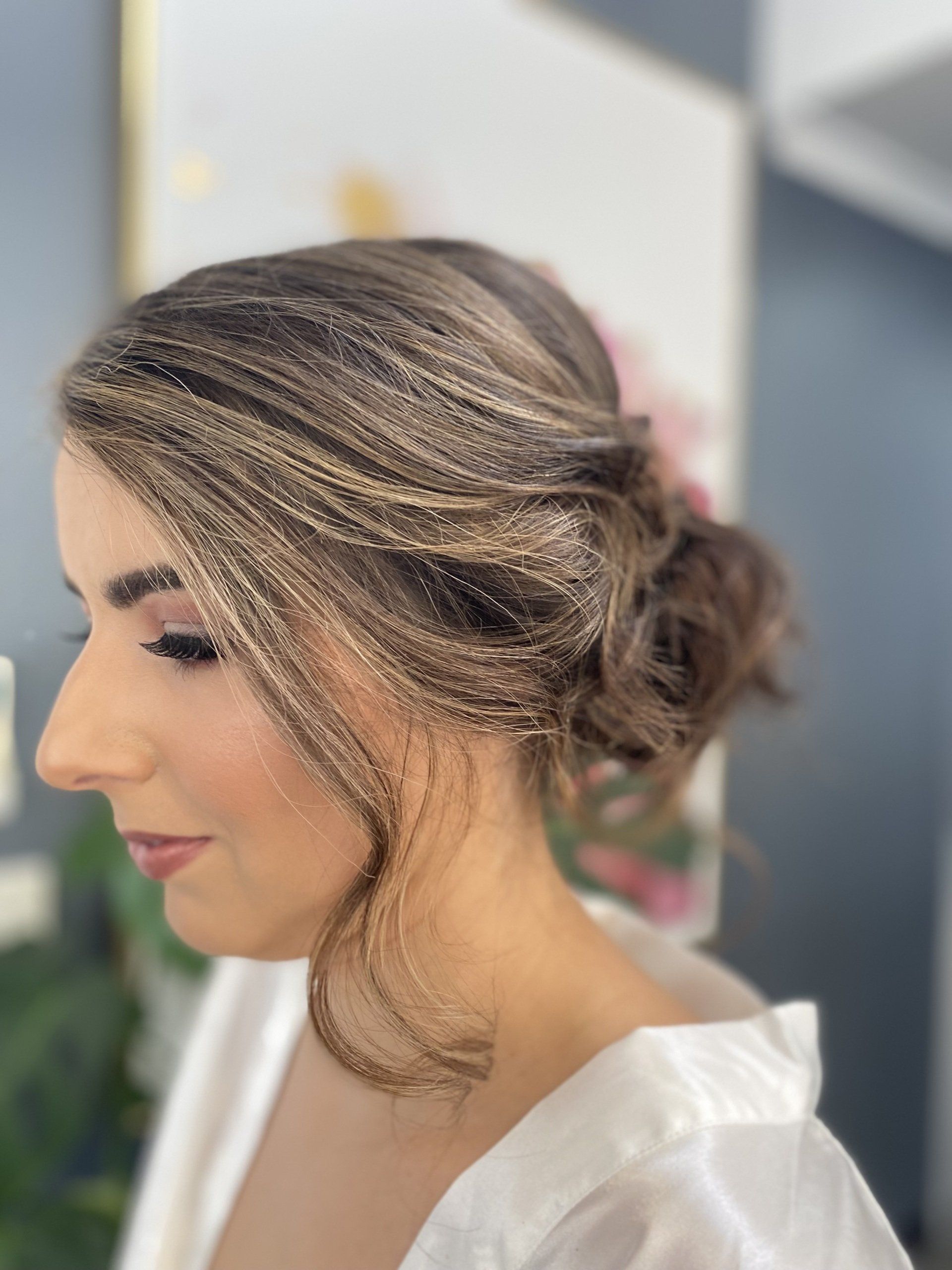 Woman with updo hairstyle, side profile. Hair features glitter strands. She wears makeup and a white robe.