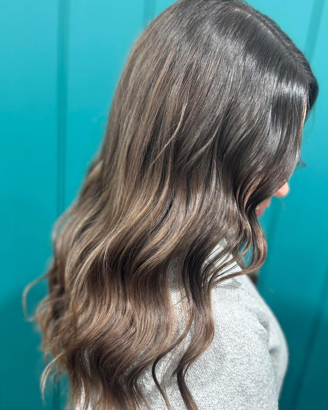 Side view of long wavy brown hair against a teal background