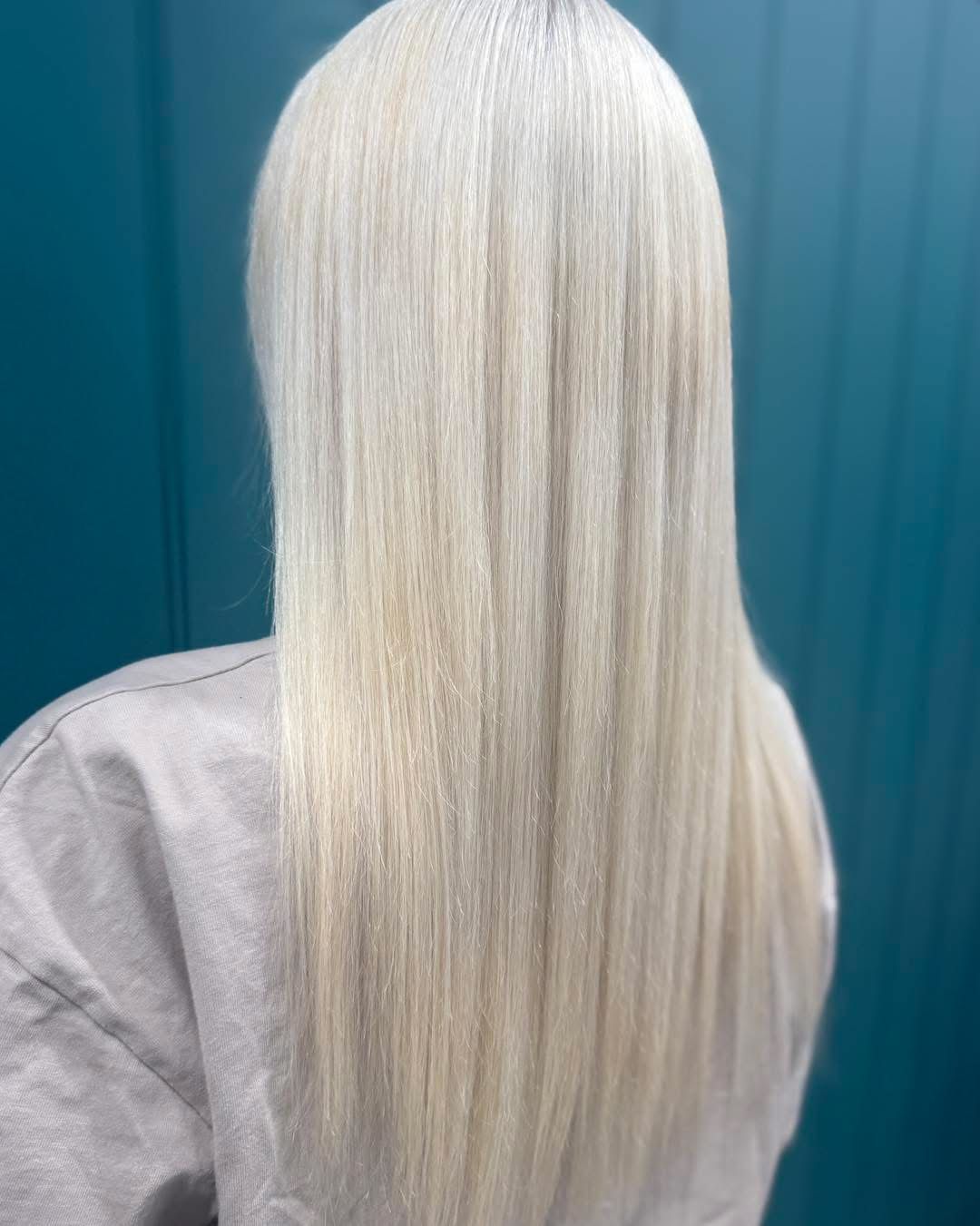 Back view of long straight platinum-blonde hair against a teal background