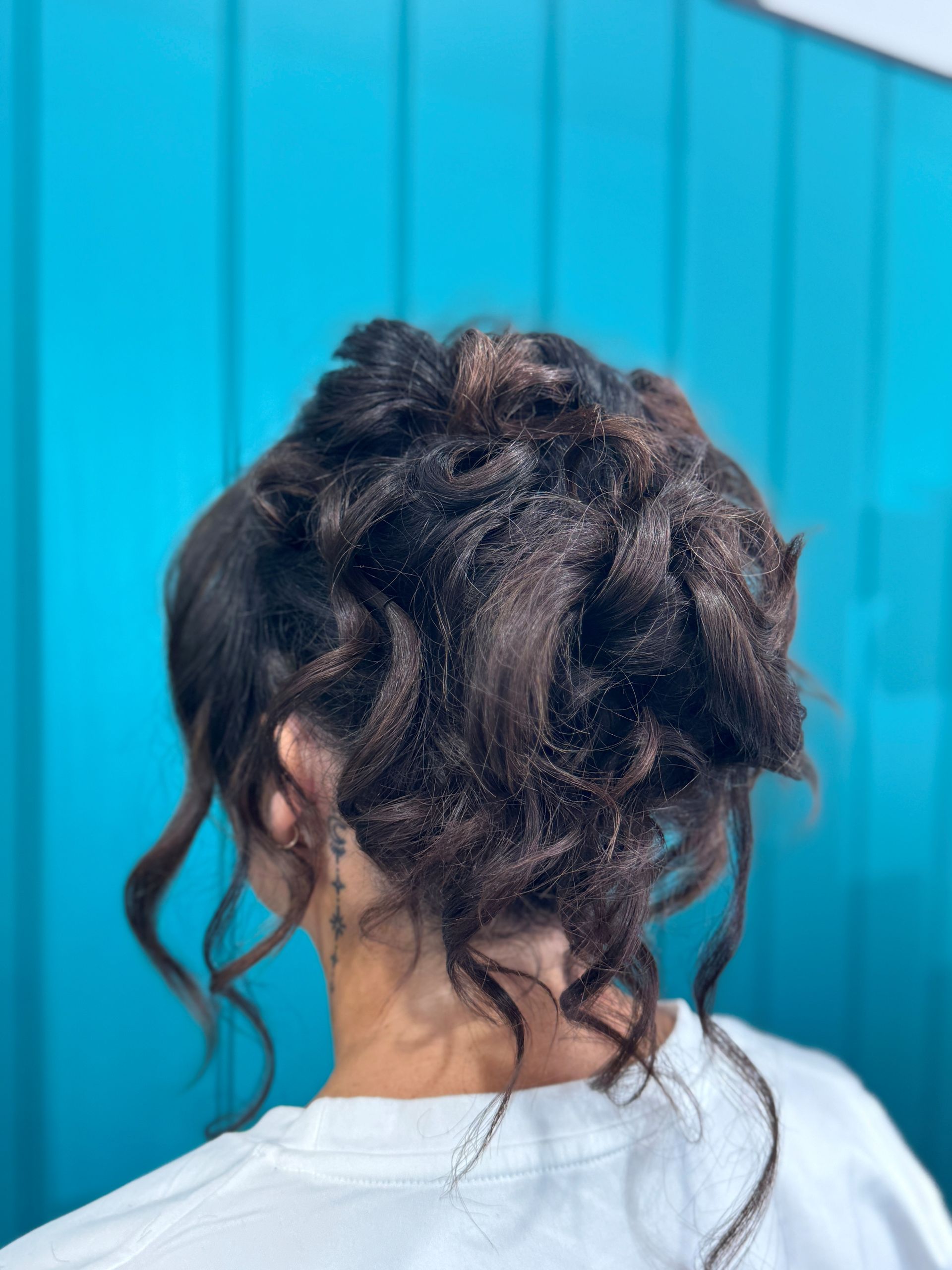 Back view of a person with curly dark hair against a bright blue wall