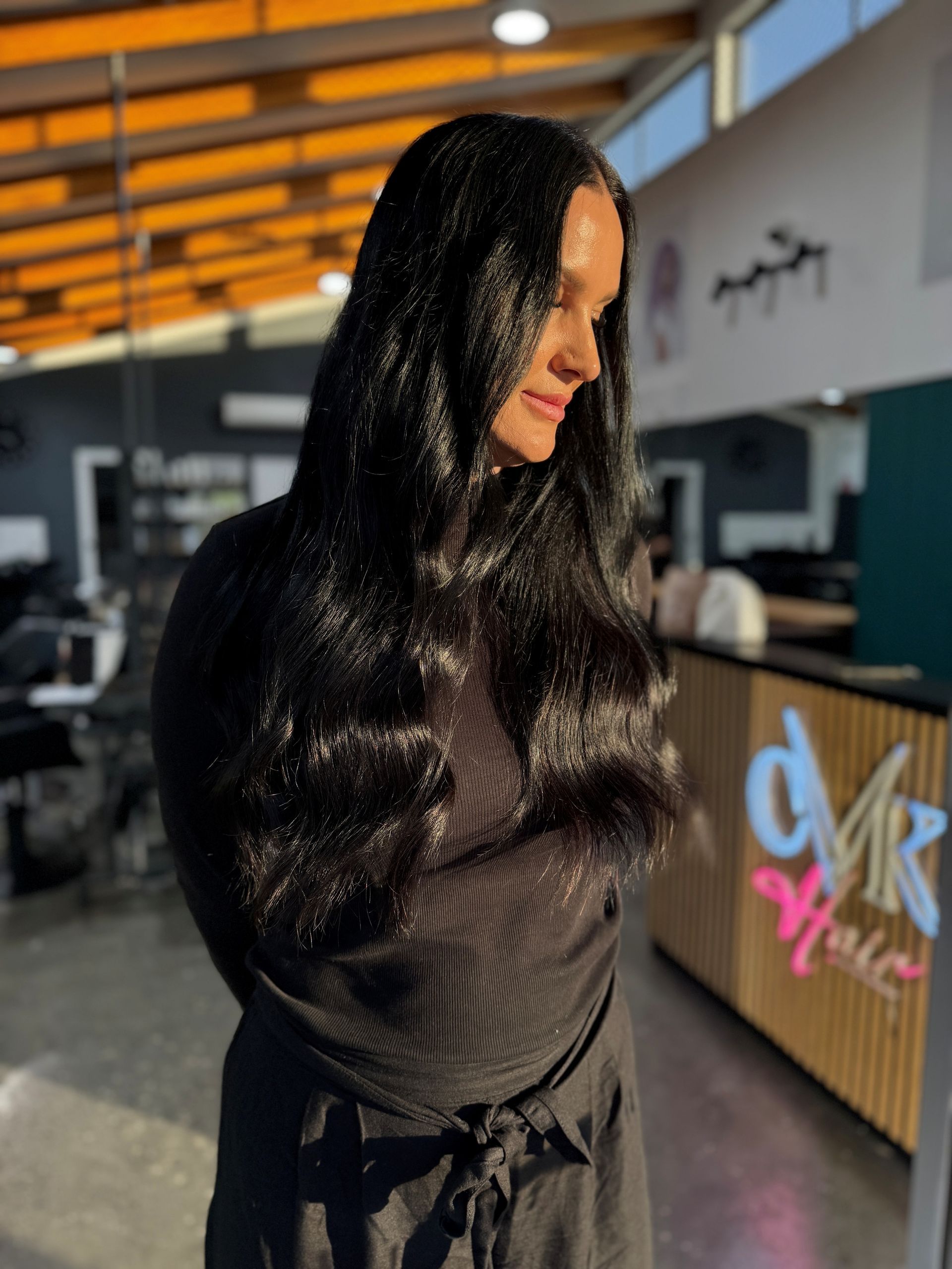 Woman with dark hair, highlights, and wavy style; wearing a black shirt.