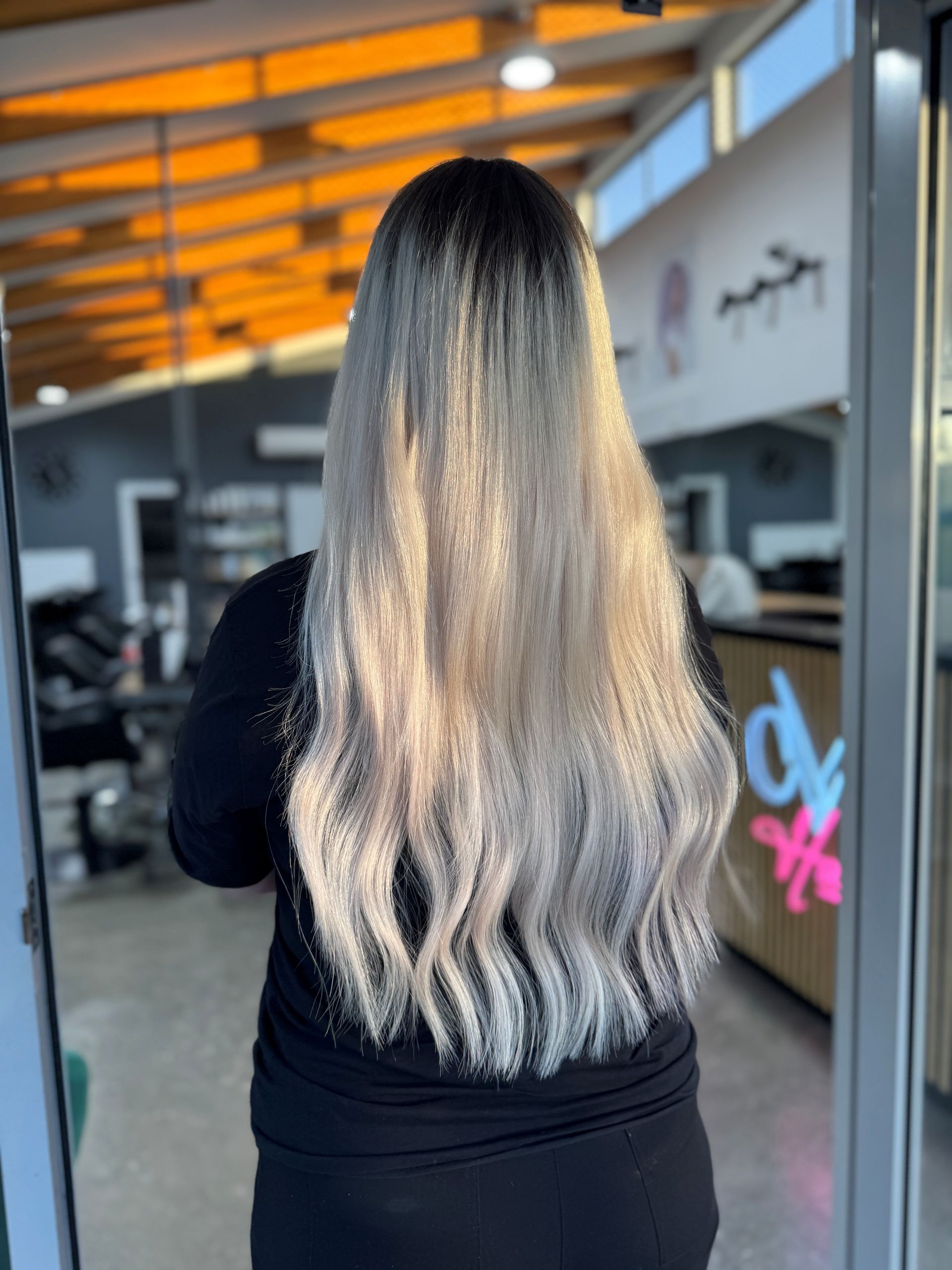 Person with long blonde ombré hair standing inside a salon or store entrance