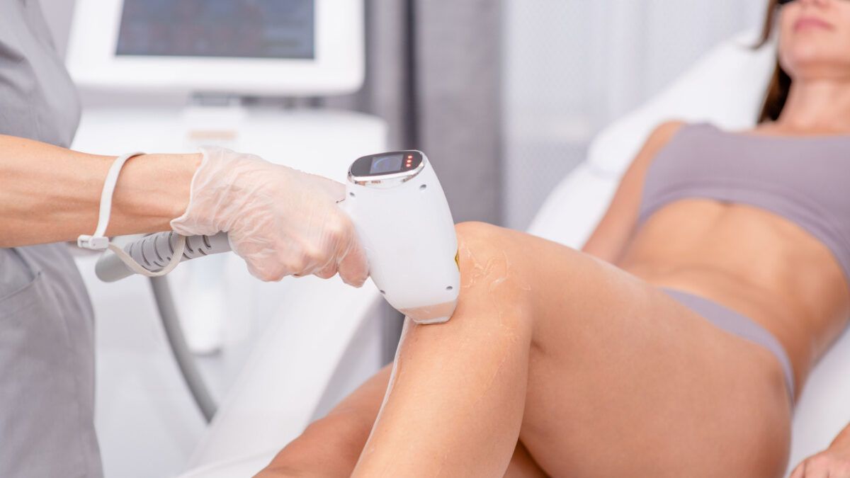 Epilazione laser sulla gamba di una persona in una clinica; la persona è sdraiata mentre il tecnico utilizza il dispositivo.