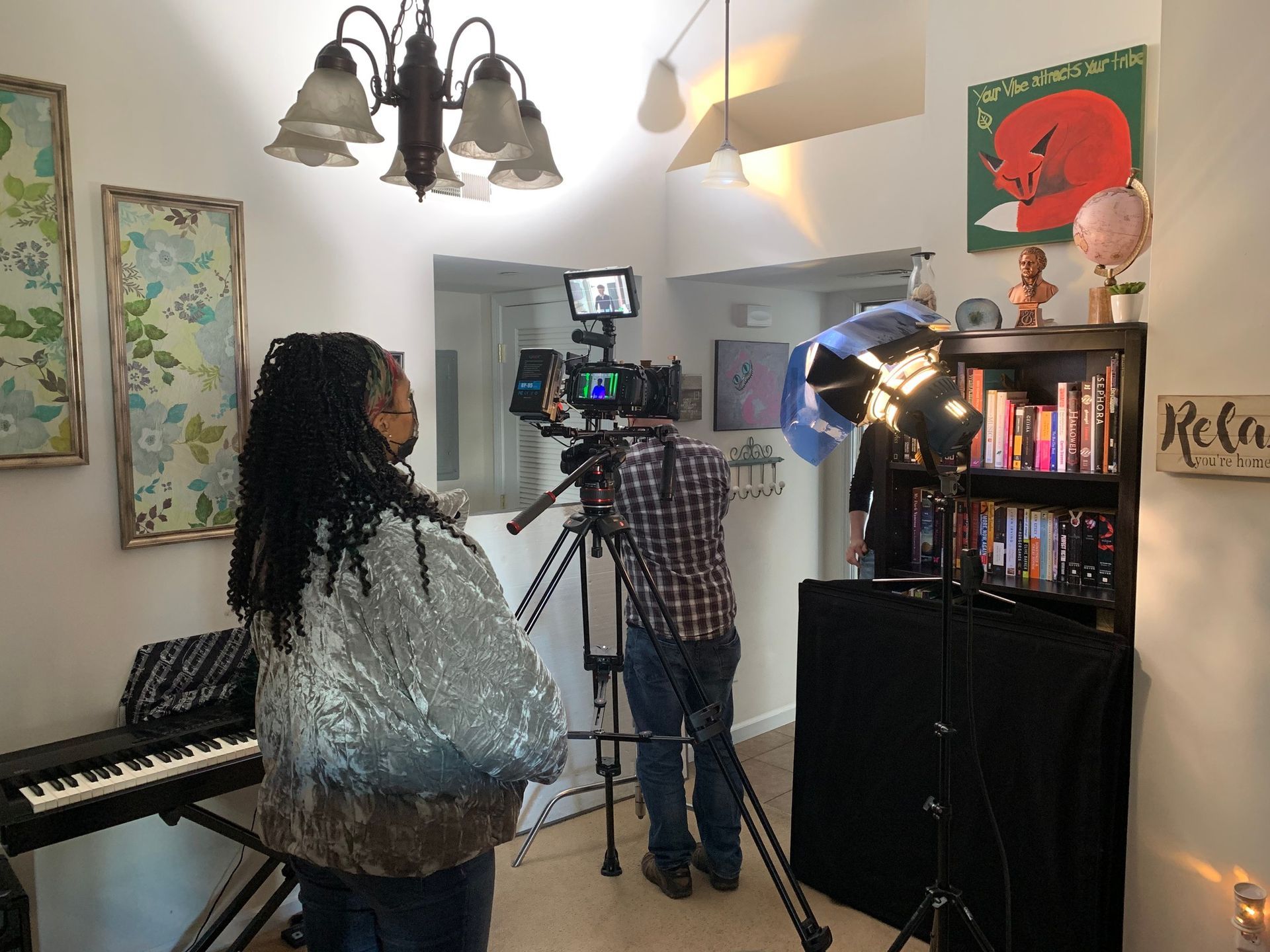 Two people filming in a living room with a camera on a tripod and bright studio lights