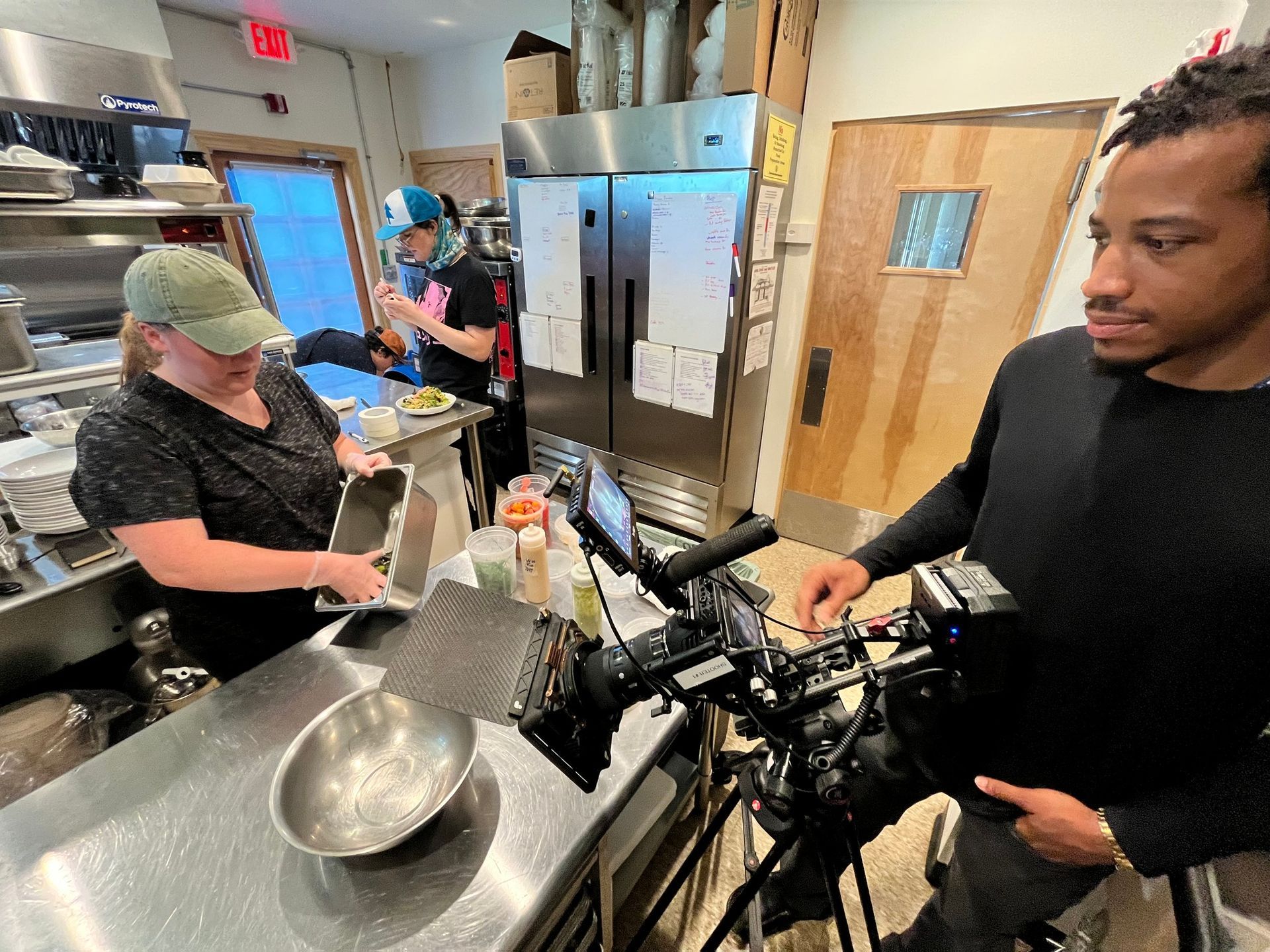 Kitchen staff preparing food beside a camera crew in a restaurant kitchen
