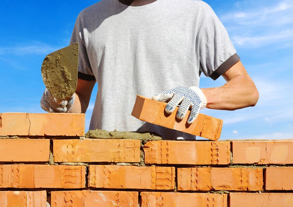 A Man Is Laying Bricks On A Brick Wall — Heritage Bricklaying & Remedial Services In Erina, NSW