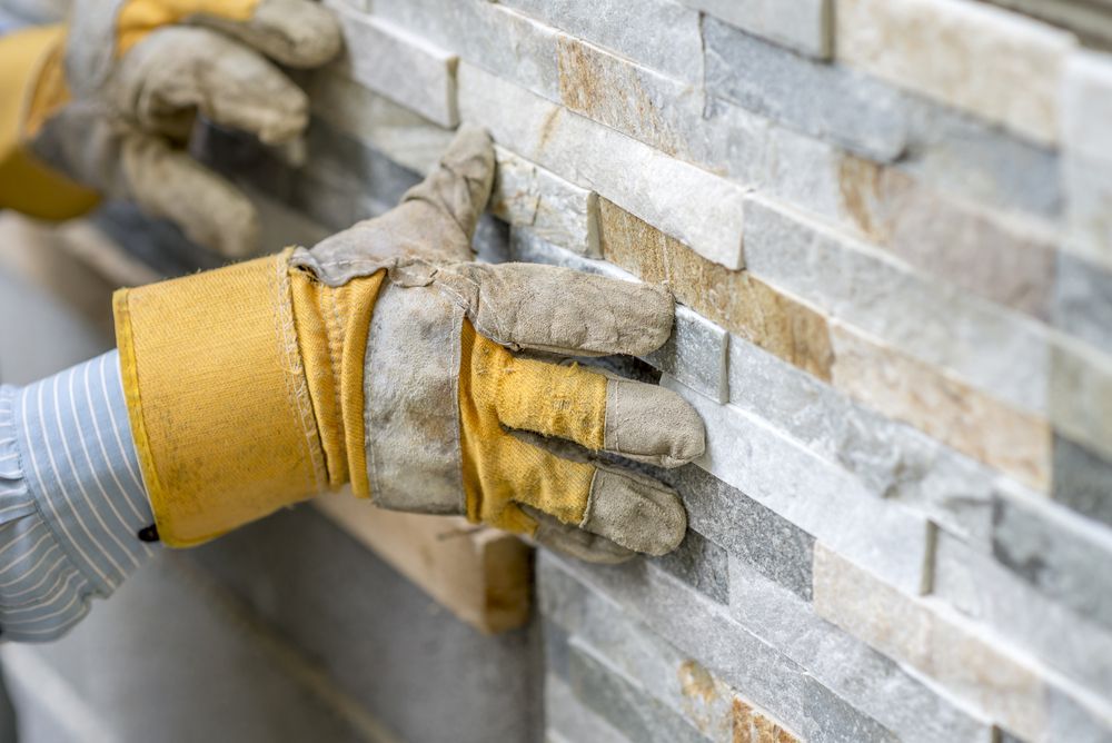 A Person Wearing Gloves Is Installing A Stone Wall — Heritage Bricklaying & Remedial Services In Terrigal, NSW