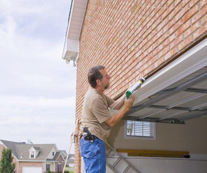 A Man Is Standing On A Ladder Fixing A Garage Door — Heritage Bricklaying & Remedial Services In Toukley, NSW