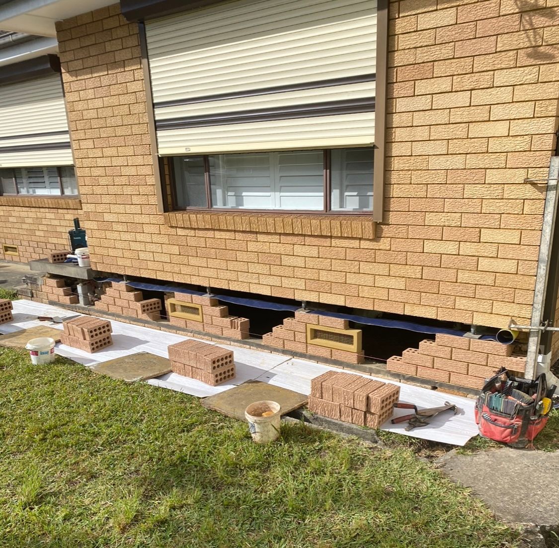 A Brick Wall With A Window And Foundation Vents Being Installed — Heritage Bricklaying & Remedial Services In Jilliby, NSW