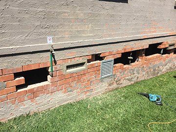 A Brick Wall With Holes In It Is Sitting On Top Of A Lush Green Lawn — Heritage Bricklaying & Remedial Services In Toukley, NSW