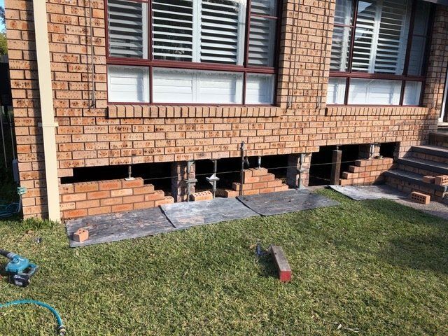 A Brick House With A Hose In The Grass In Front Of It — Heritage Bricklaying & Remedial Services In Toukley, NSW