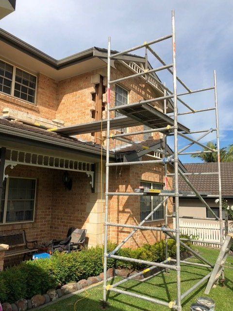 A Scaffolding Is Sitting In Front Of A Brick House — Heritage Bricklaying & Remedial Services In Jilliby, NSW