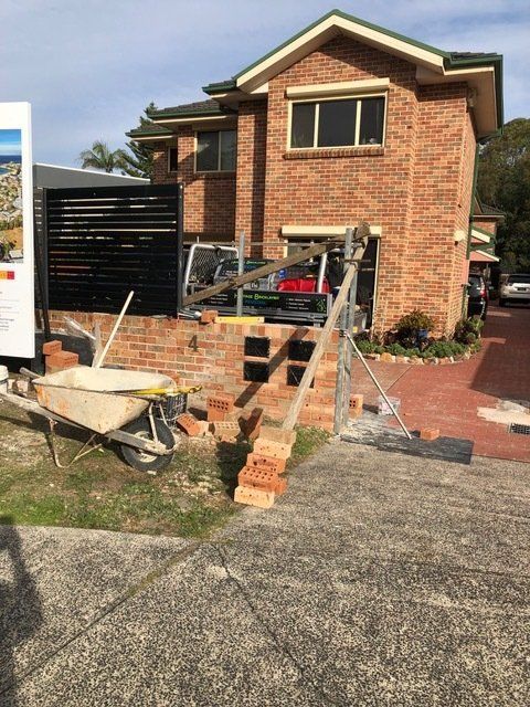 A Brick House With A Wheelbarrow In Front Of It — Heritage Bricklaying & Remedial Services In Jilliby, NSW
