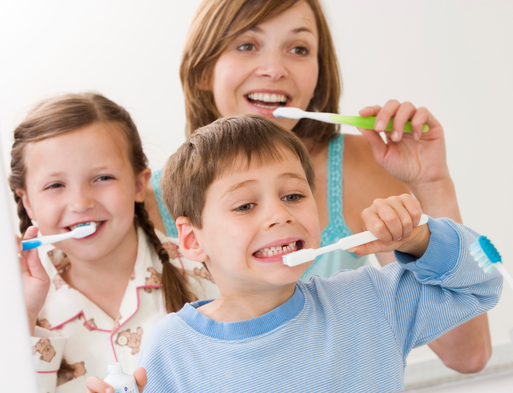 mom and two children smiling and brushing teeth | General dentist for cleanings, fillings, and more in Friendswood TX