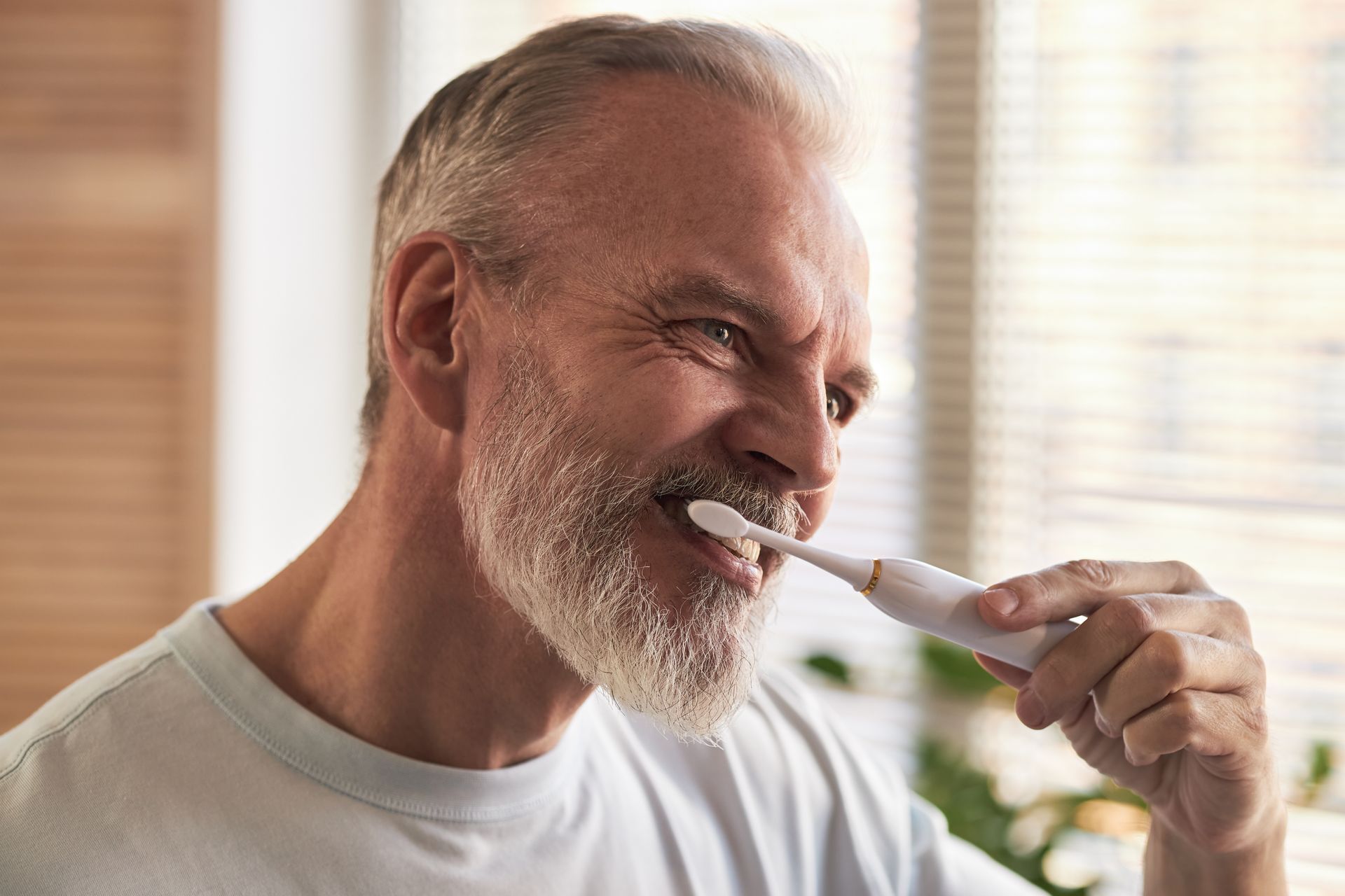 Man brushing his teeth in a bright bathroom with a white toothbrush and sink in the background