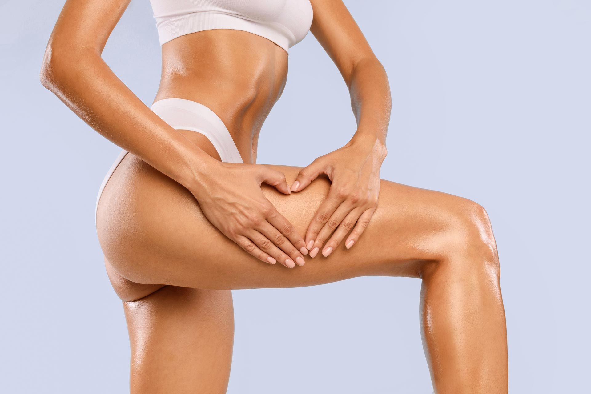Person in white underwear applying body lotion to thigh against a light background