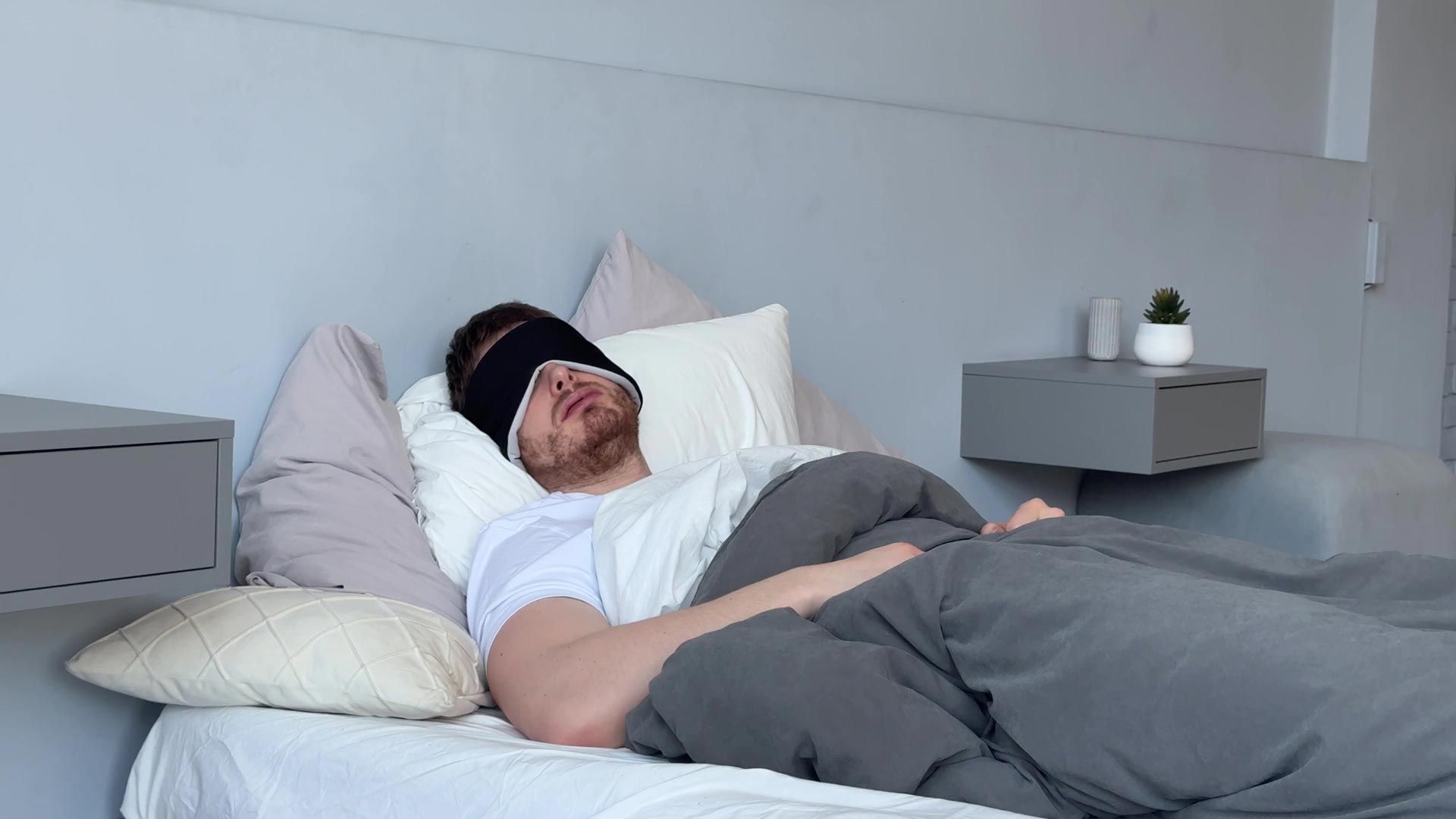 Man resting in bed under gray blanket in a bright, minimalist bedroom