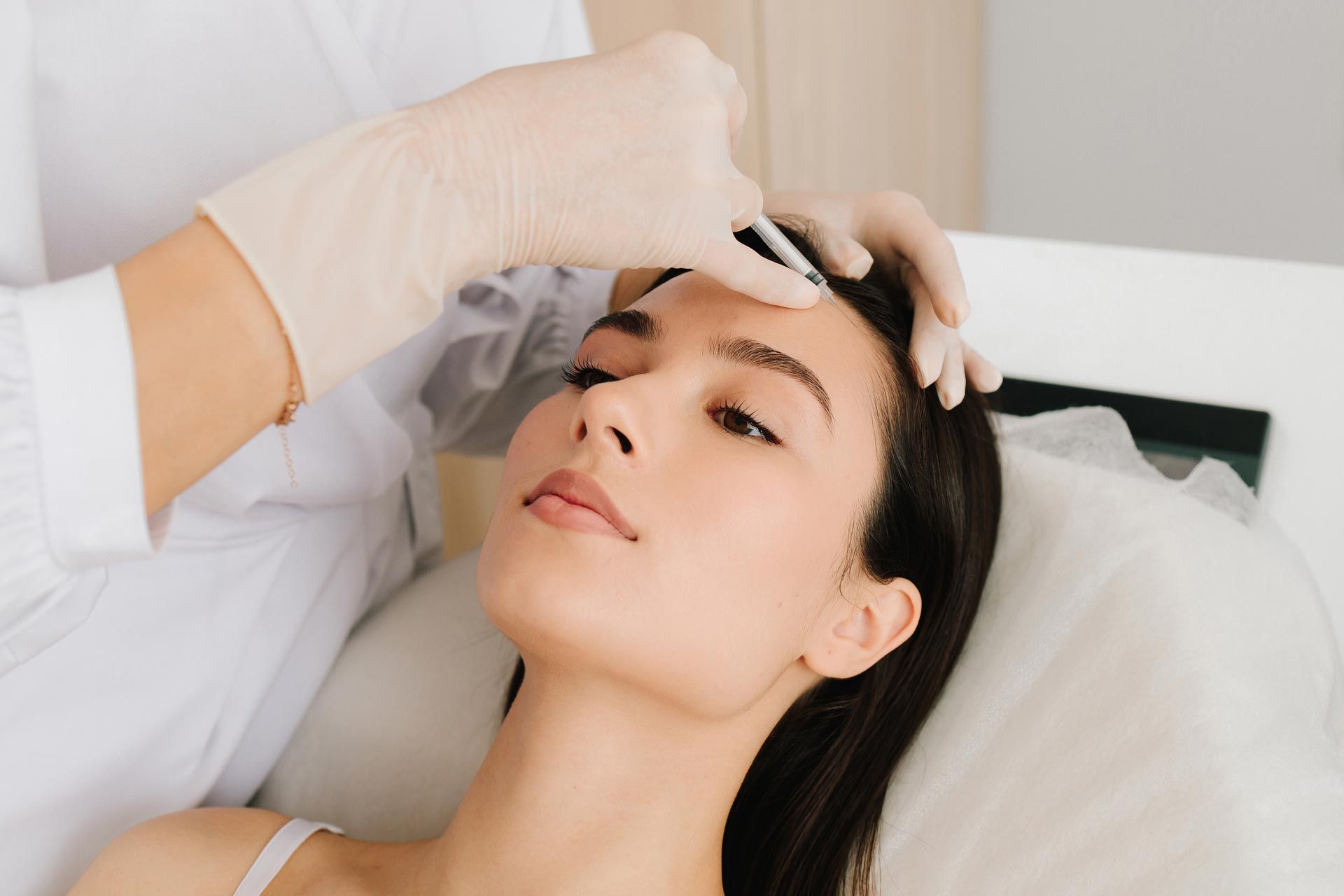 Gloved hand applying treatment to a woman's forehead in a clinic setting