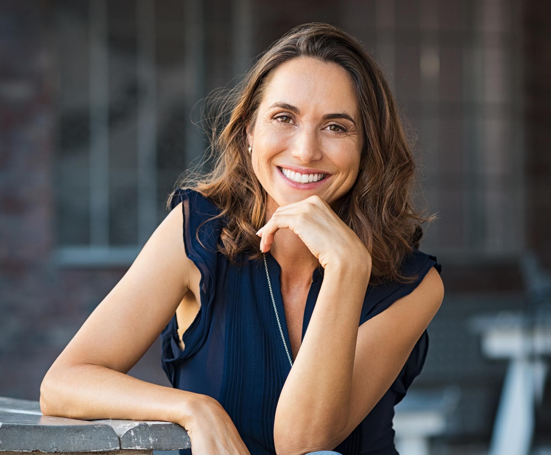 Smiling woman in a navy blouse leaning on a railing outdoors