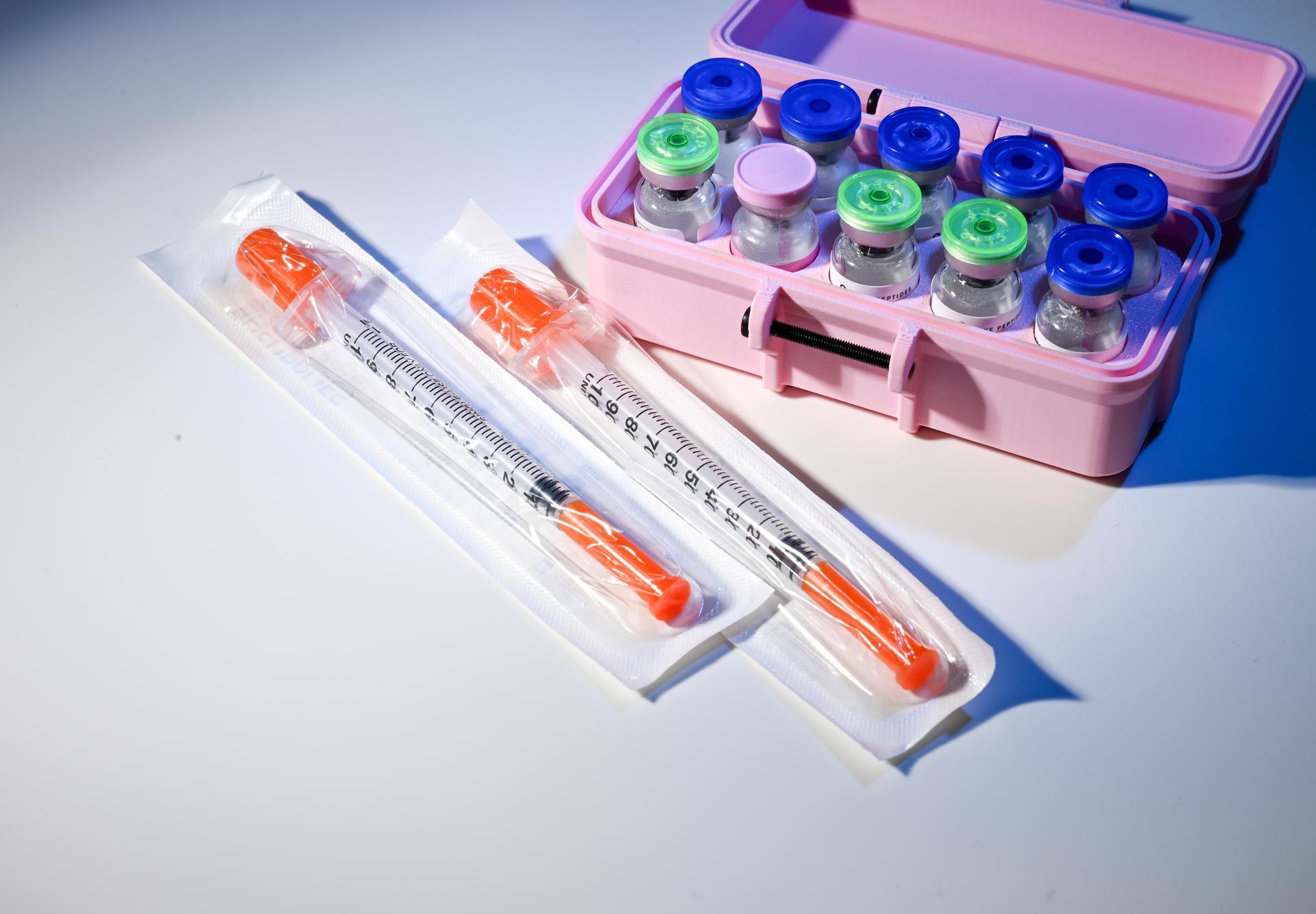Medical vials in a pink carrying case beside two syringes in sterile packaging