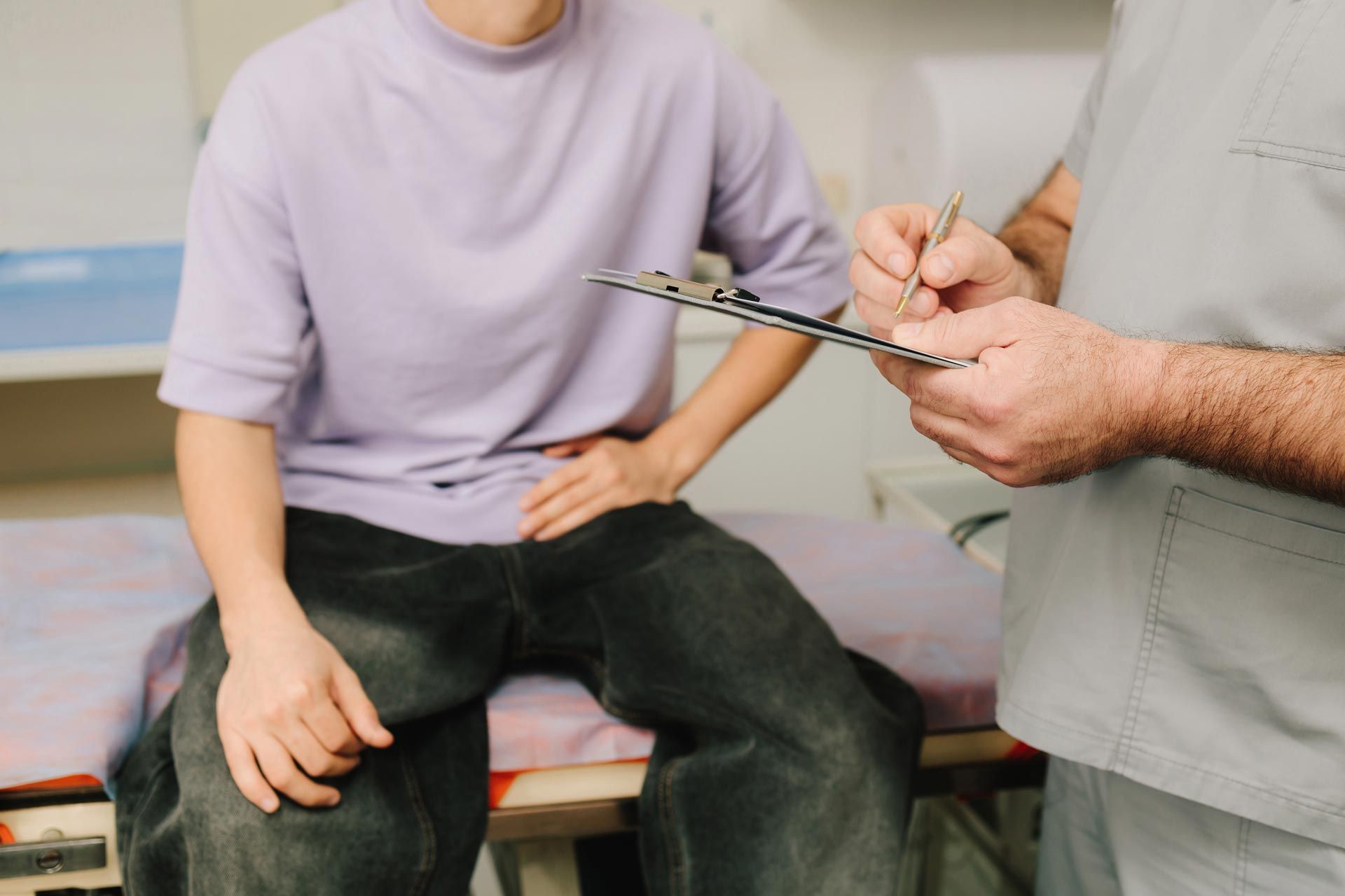 Person seated on a medical exam table while a clinician takes notes on a clipboard