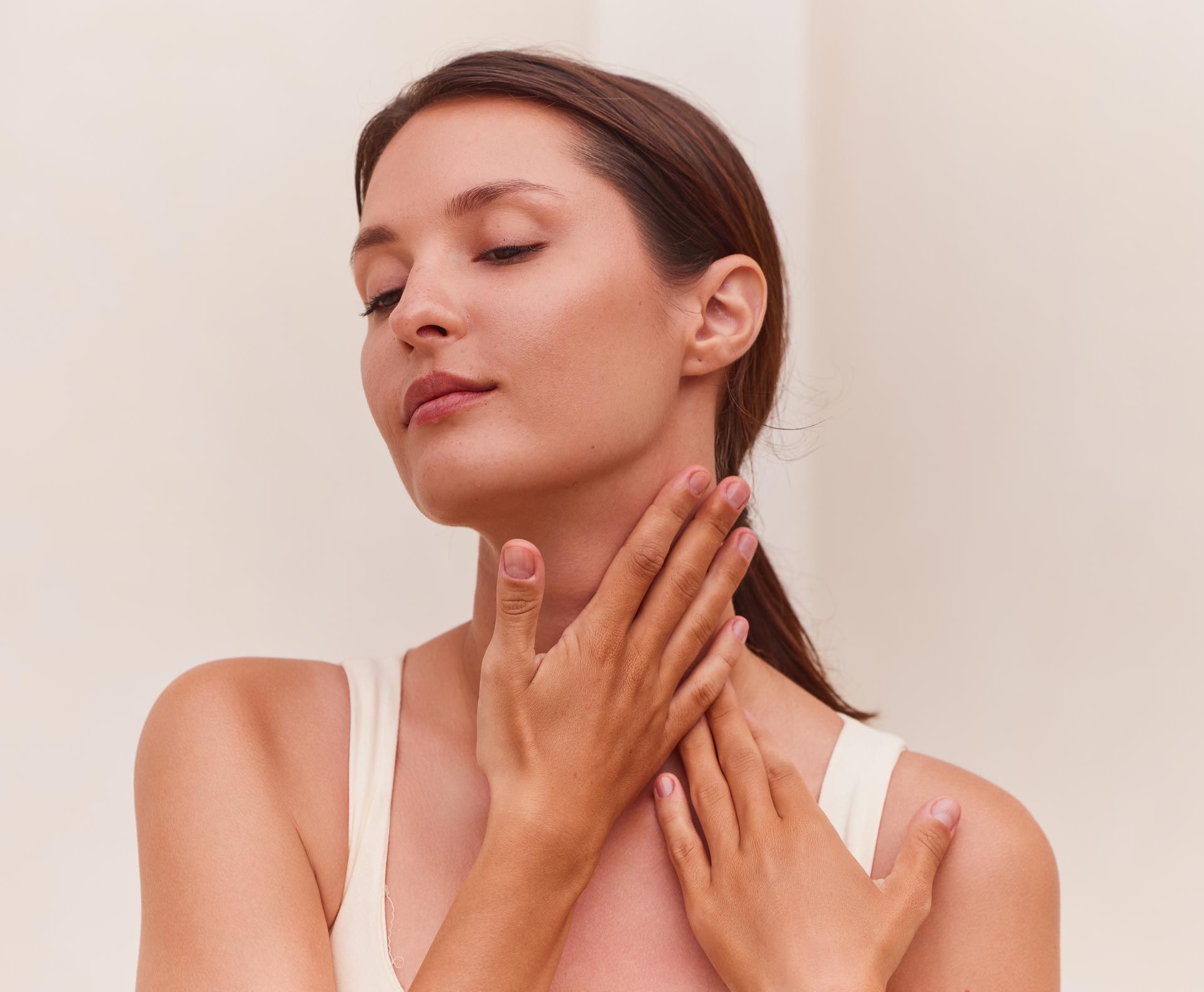 Woman gently touching her neck and jaw, eyes closed, against a light background.
