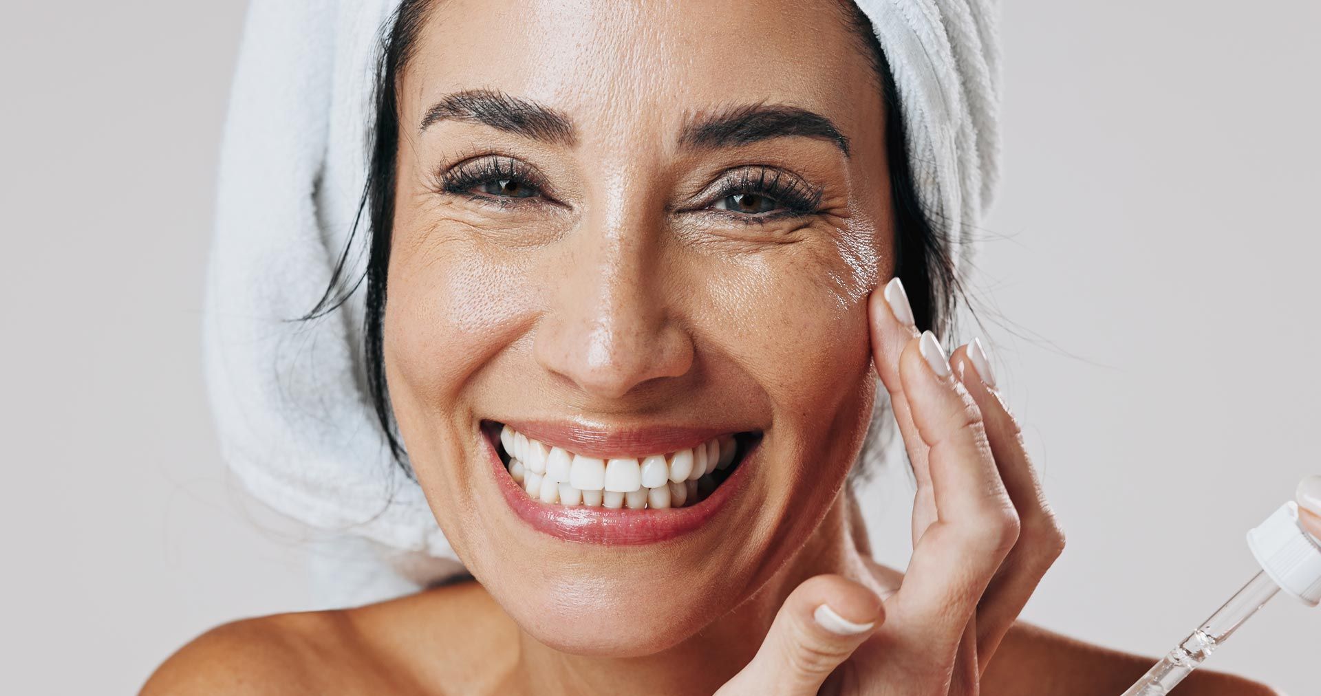 Smiling woman applying skincare cream to her face with a white applicator