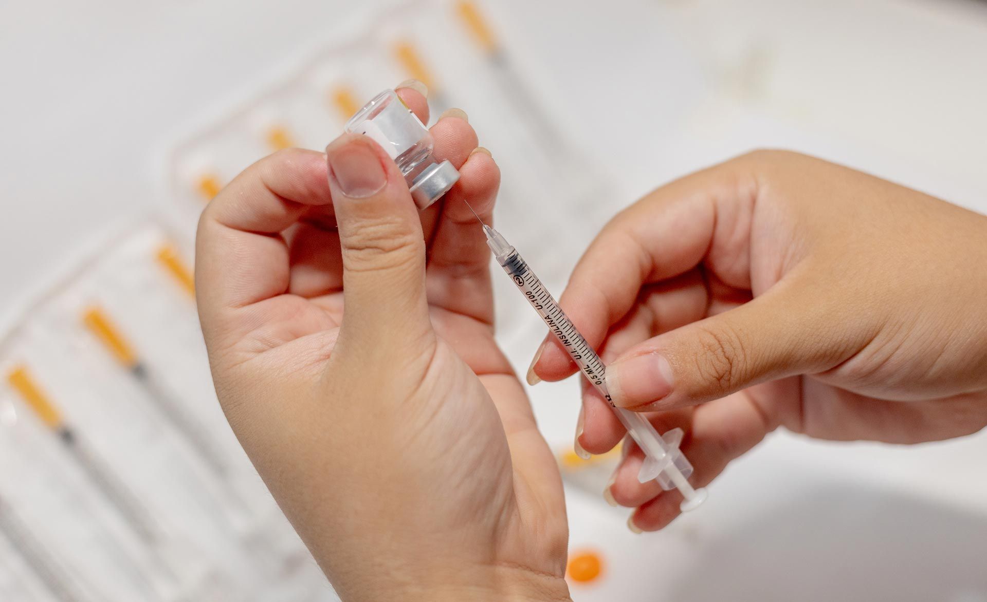 Hands drawing vaccine from a vial into a syringe over a white background