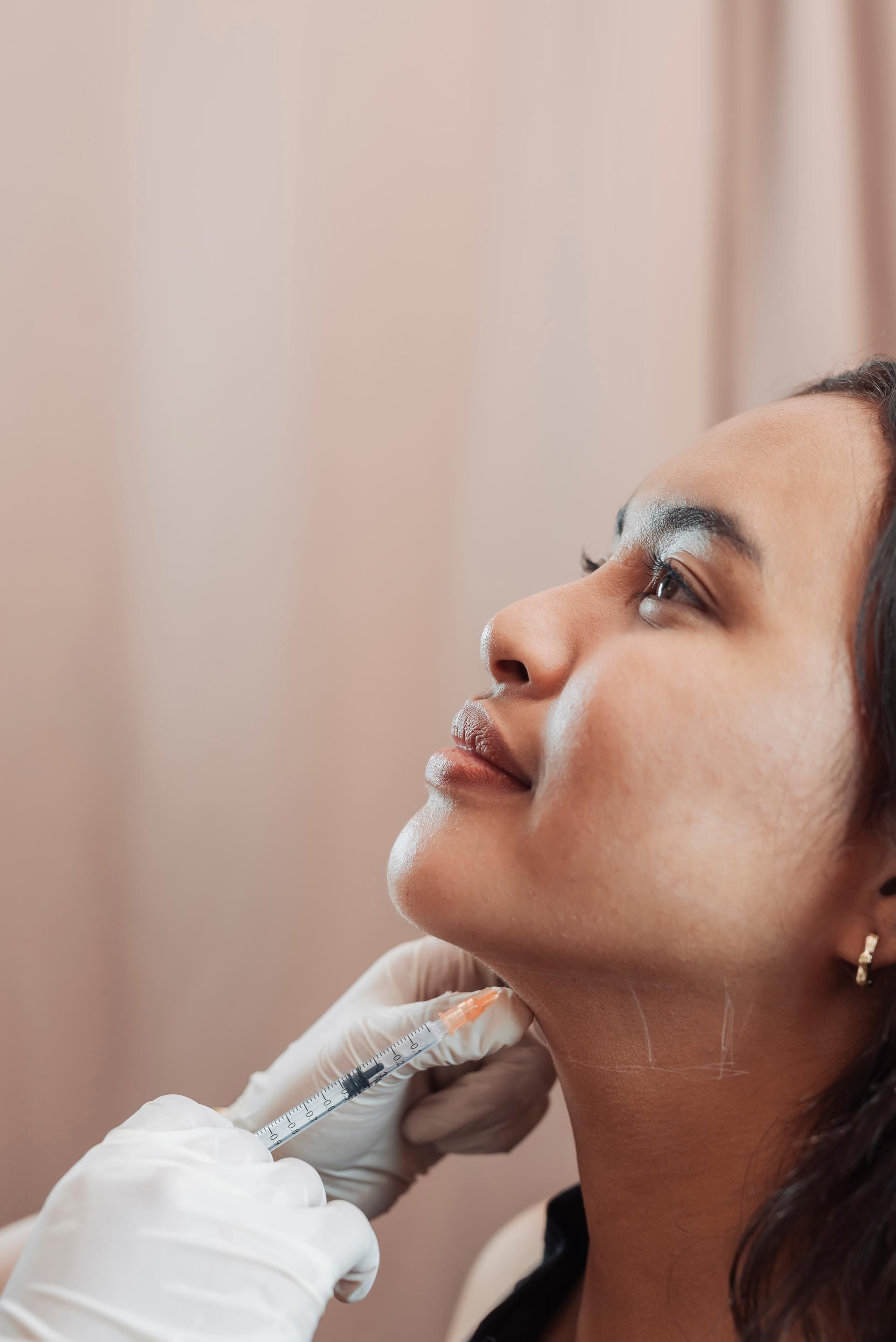 Close-up of a woman receiving a facial treatment with a gloved hand against a soft beige background