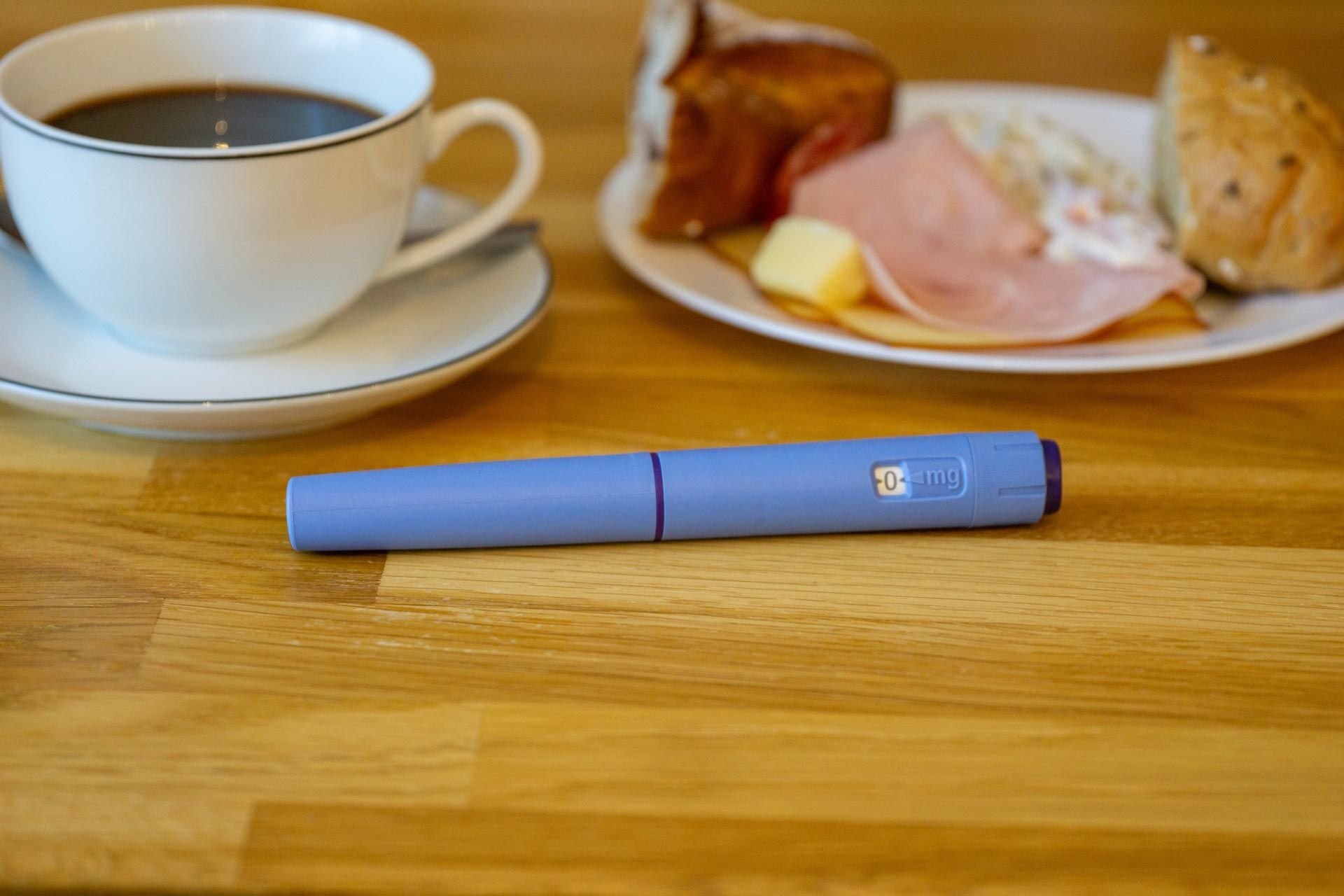 Blue lipstick on a wooden table beside a coffee cup and a plate of pastries