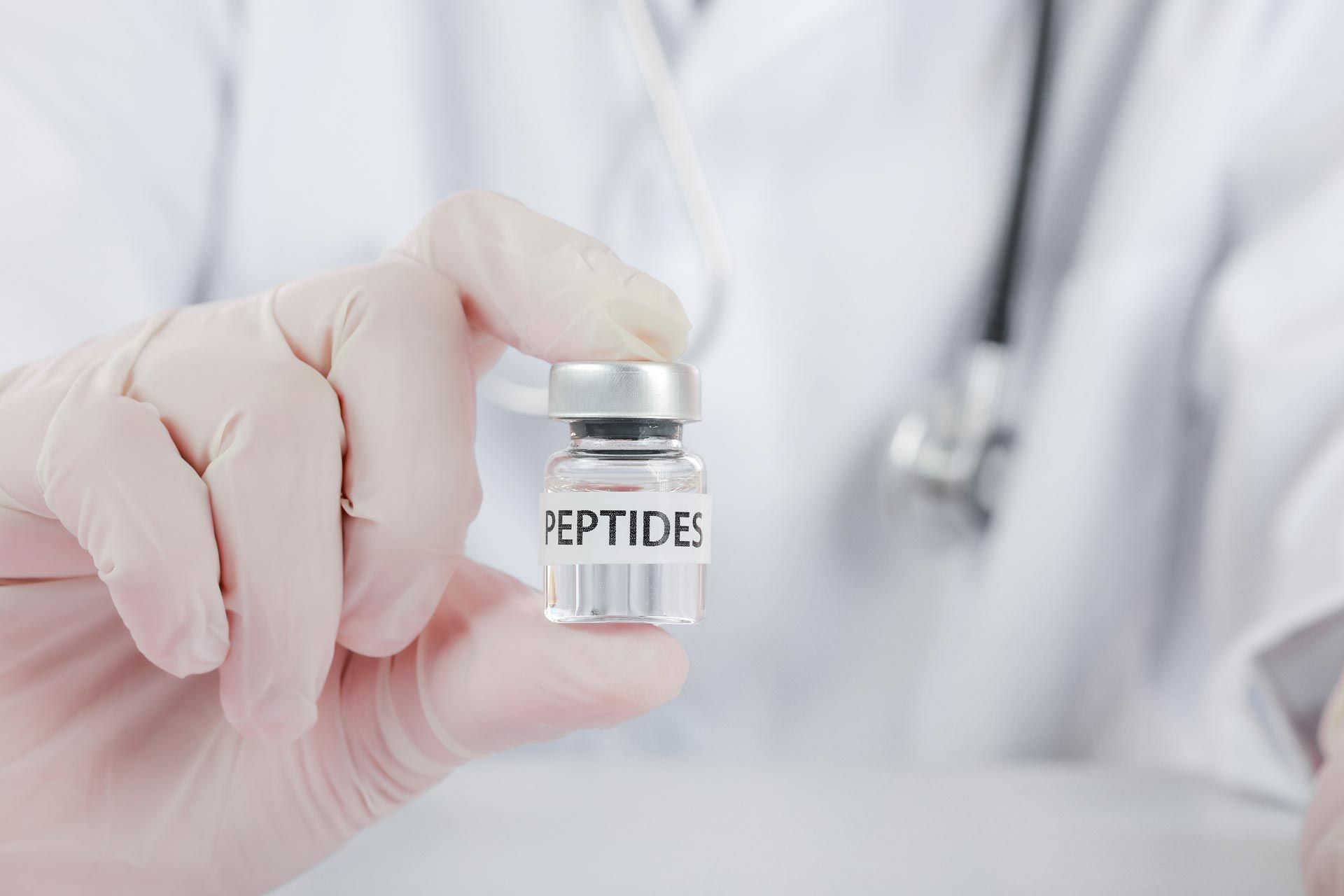 Gloved hand holding a small vial labeled “PEPTIDES” against a white lab coat background