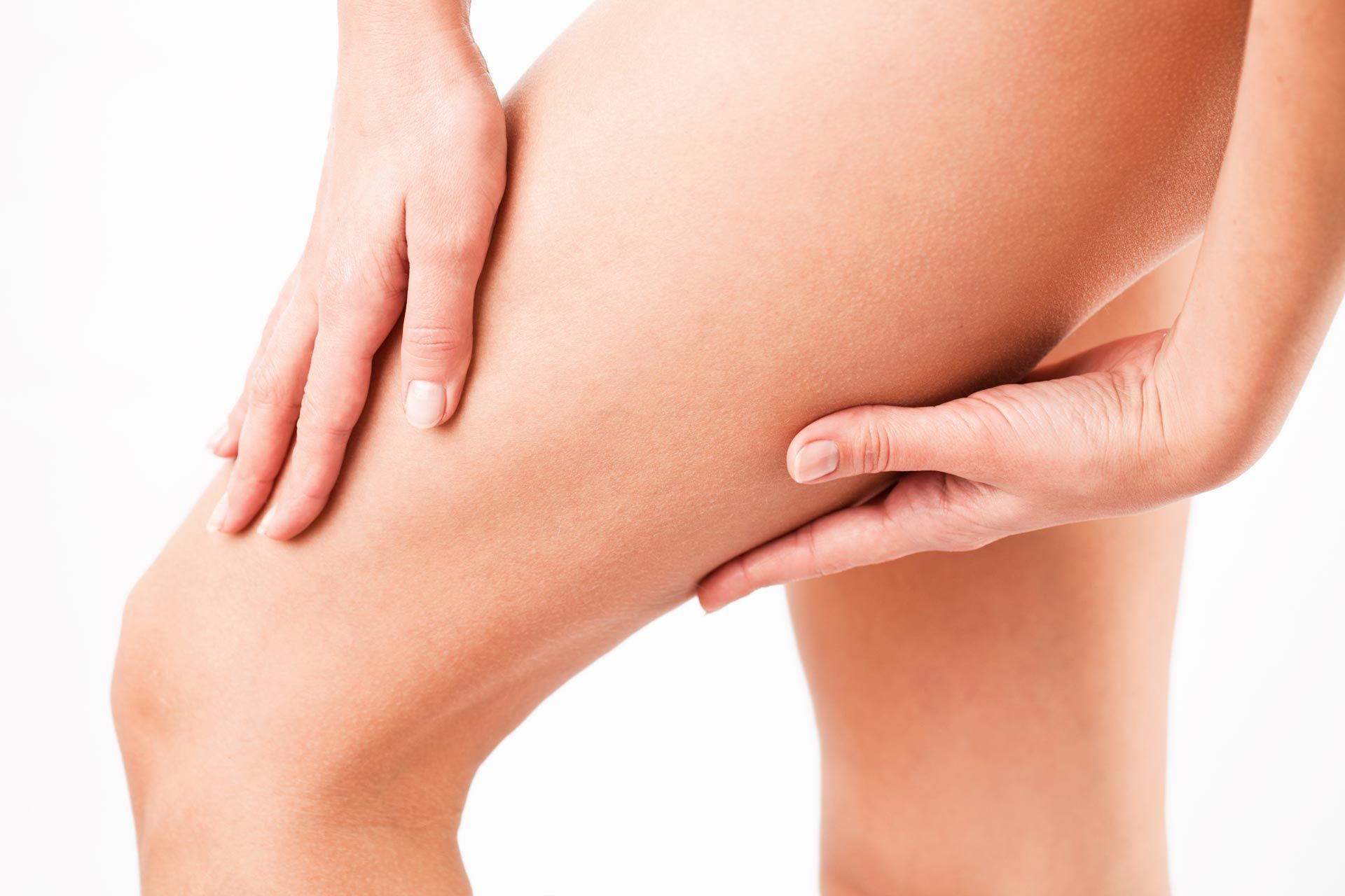Hands pinching thigh skin on a person’s leg against a white background