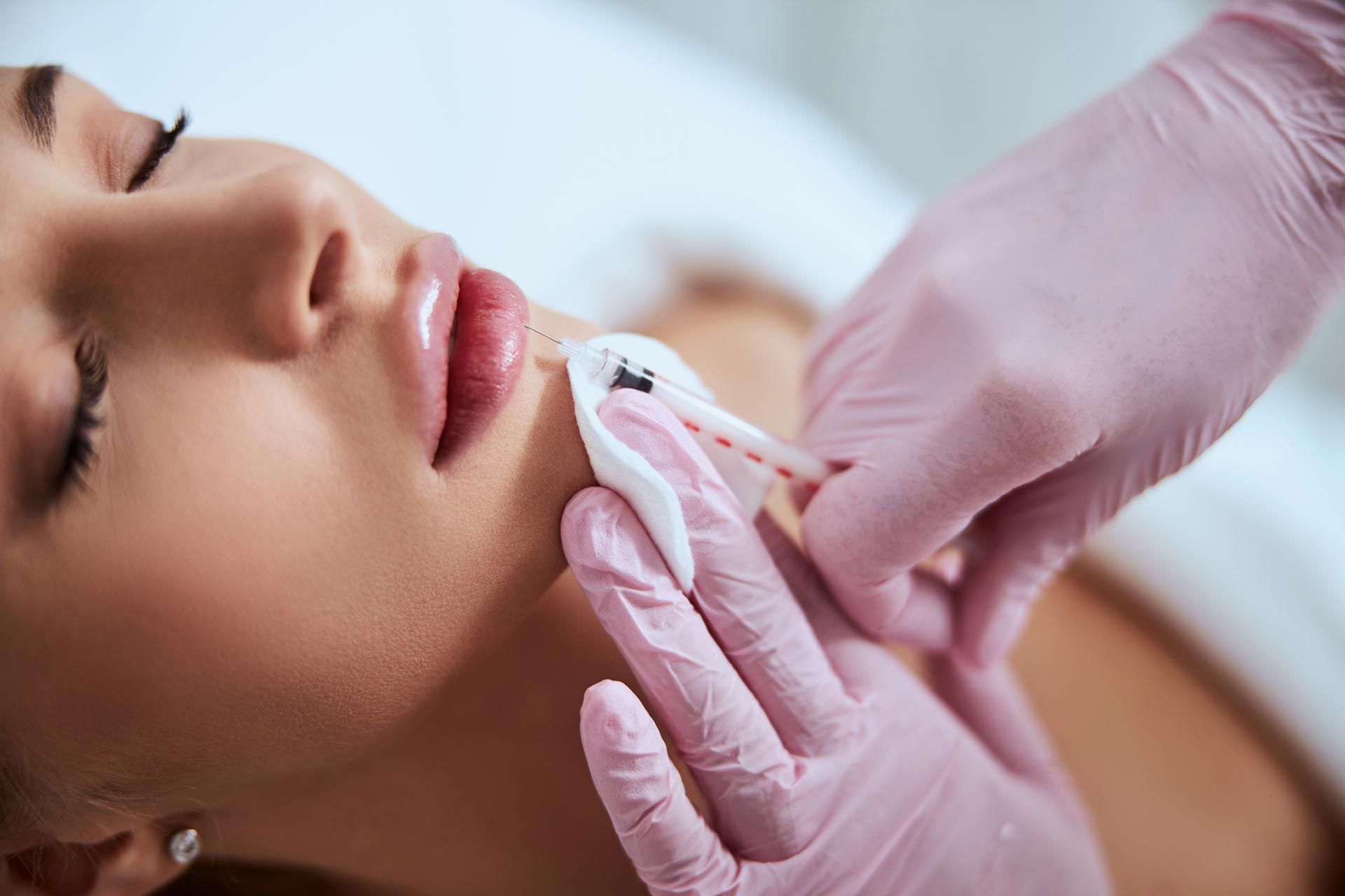 Gloved hands injecting filler into a woman’s chin during a cosmetic procedure