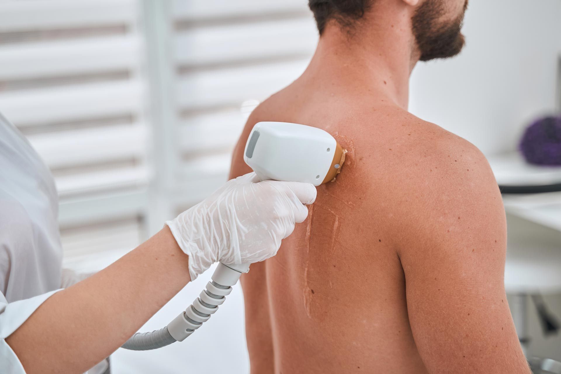 Gloved technician using a handheld laser device on a man’s upper back in a clinic
